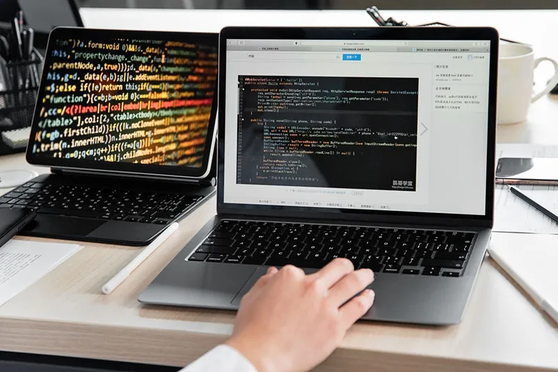 A developer writing code on a laptop, displaying programming scripts in an offic